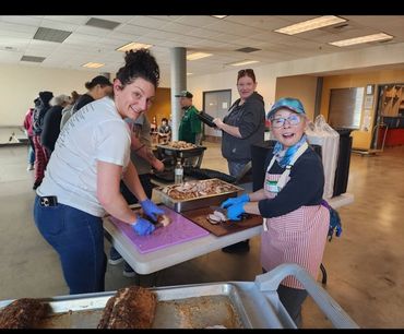 (Volunteers packing food):Community members working together with smiles to portion out warm, nutritious meals.